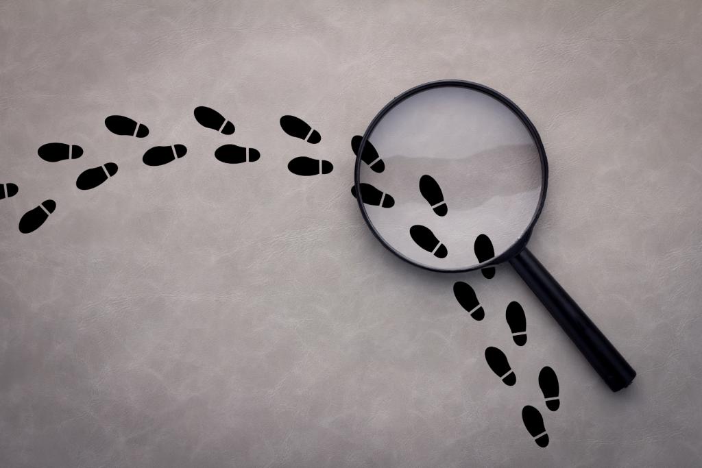 Magnifying glass over footsteps on grey background